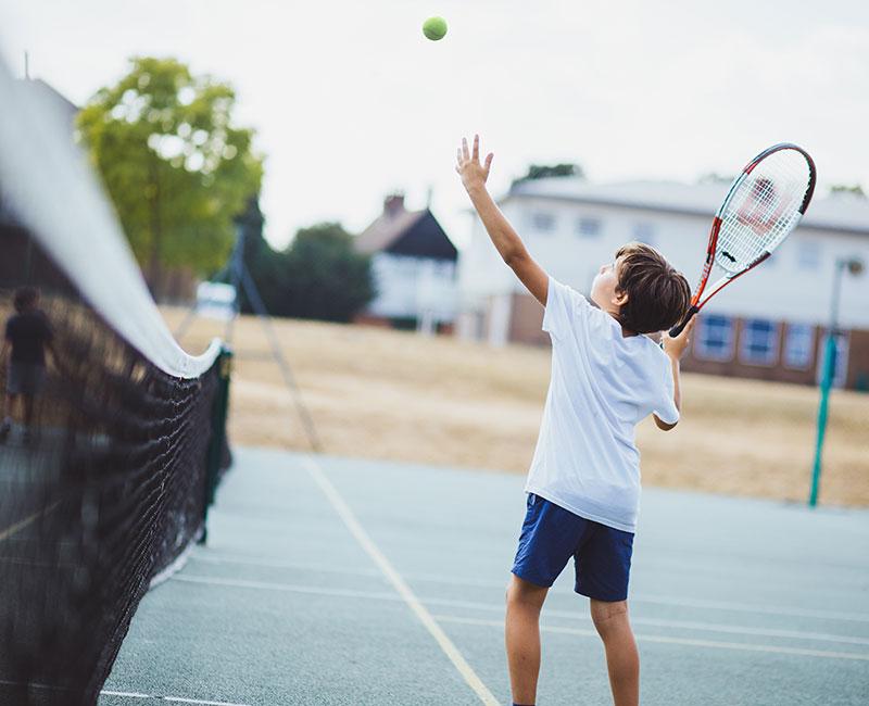 Ein Junge macht auf England Sprachreise beim Tennis einen Aufschlag