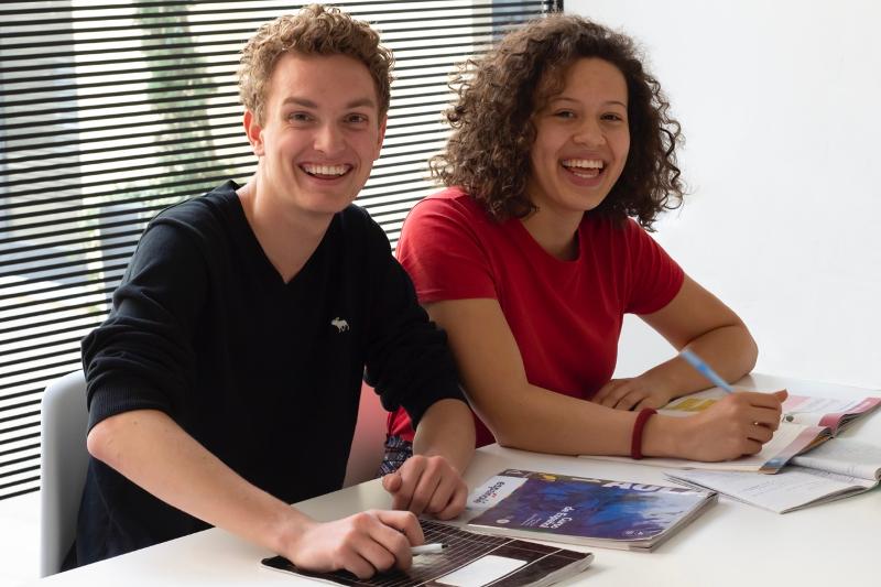 Zwei Jugendliche lachen in die Kamera beim lernen