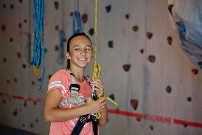 Ein Mädchen mit Lächeln im Gesicht steht auf Sprachreise vor Kletterwand