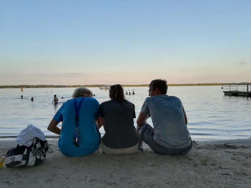 Betreuer und Teilnehmer der Sprachreise sitzen am See und schauen den Sonnenuntergang