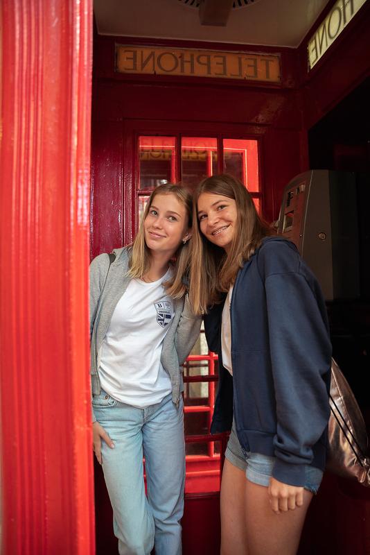 Zwei Freundinnen stehen auf Sprachreise England günstig in einer Telefonzelle