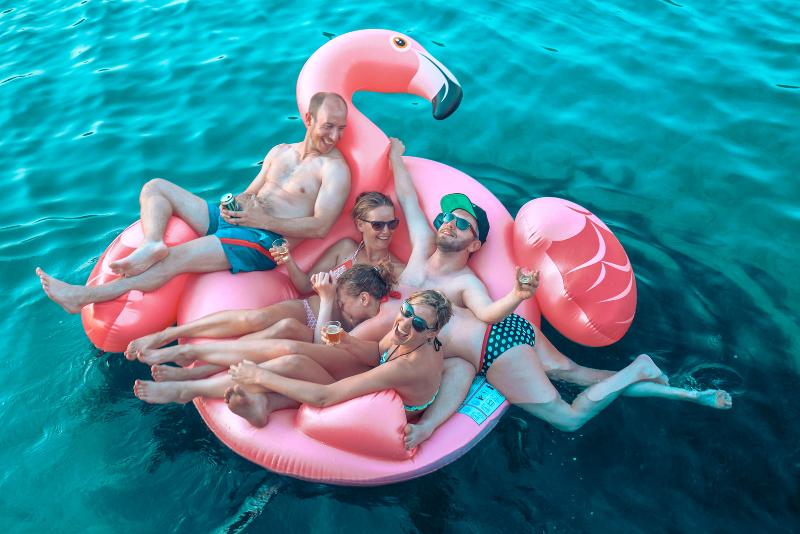 Teilnehmer einer Jugendreise ab 18 sitzen auf einem Schwimm-Flamingo
