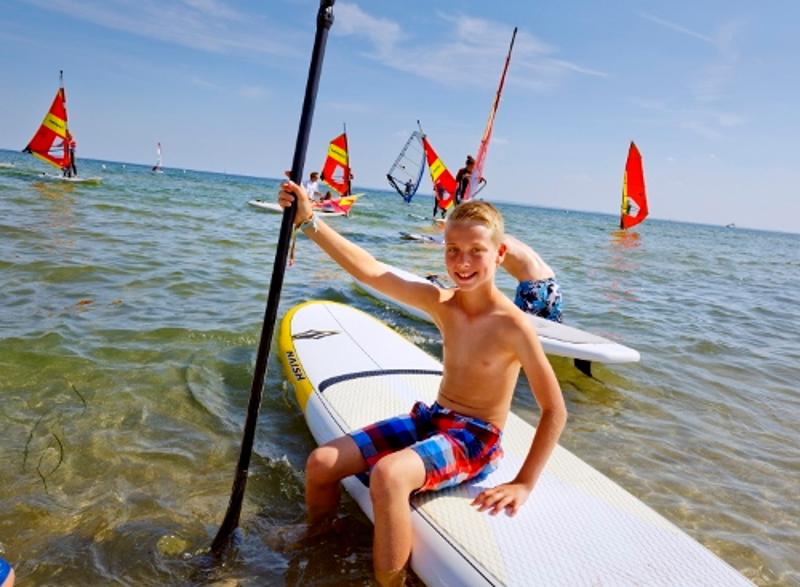 Junge sitzt auf Surfbrett im Wasser im Ostsee Jugendurlaub