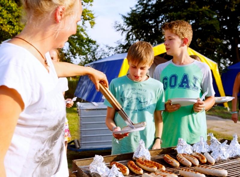 Jungs tun sich gegenseitig Würste vom Grill auf im Ostsee Jugendurlaub