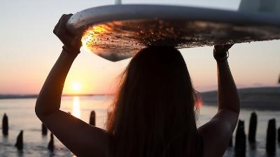 Mädchen trägt Surfbrett am Strand auf dem Kopf