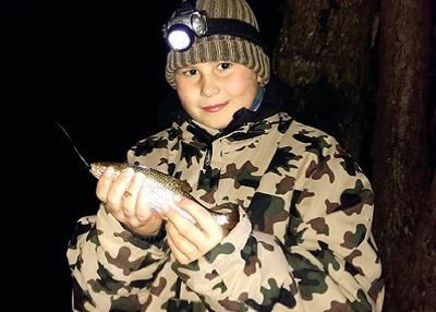 Junge in Tarnkleidung hält Fisch im Dunkeln im Herbst im Loppin Angelcamp Ferienlager