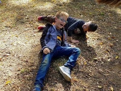 Zwei Jungs lachen auf dem Waldboden auf der Ferienfreizeit in Belgien