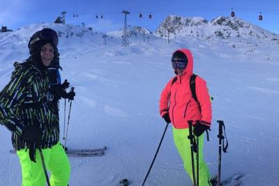 Zwei Jugendliche posieren auf Skiern auf einer Piste im Salzburger Alpenland mit einer Seilbahn im Hintergrund
