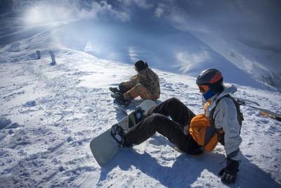 Zwei Jugendliche sitzen auf einem Berghang im Salzburger Alpenland mit festgeschnallten Snowboards im Schnee