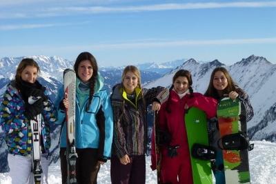Jugendliche Mädchen posieren mit ihren Skiern und Snowboards bei strahlendem Sonnenschein vor dem schneebedeckten Panorama des Salzburger Alpenlands