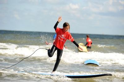Teilnehmer eines Windsurfcamps fallen vom Board