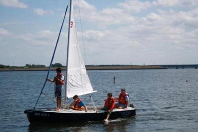 Mehrere Kinder teilen sich gemeinsam ein Boot, mit dem sie im Segelcamp über das Wasser fahren.