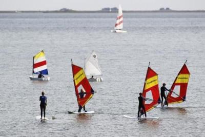 Die Teilnehmer vom Windsurfcamp versuchen sich unter Anleitung eines Trainers im Windsurfen.