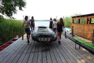Ein paar Kinder tragen während der Ferienbetreuung Sommerferien ein Schlauchboot zum Wasser