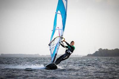 Ein Junge surft in eleganter Pose im Windsurfcamp mit dem Segel in der Hand über das Wasser.