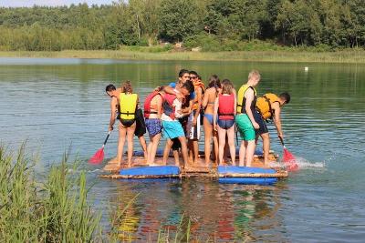 Viele Kinder treiben im Outdoor Camp über das Wasser auf ihrem Floß