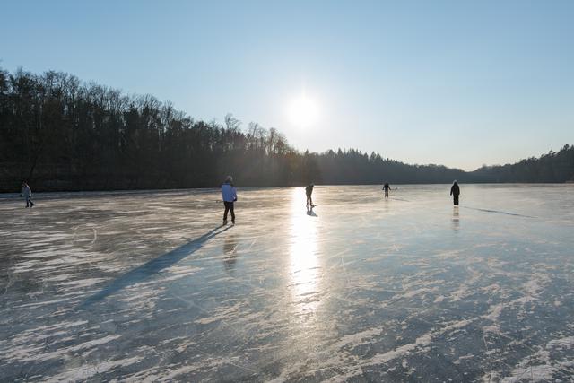 Kinder laufen unter der Wintersonne Schlittschuh auf einem zugefrorenen See im Feriencamp Brandenburg
